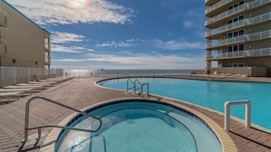 A swimming pool with a curved edge, surrounded by a brick walkway and a white fence.