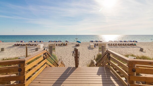 A wooden boardwalk leading to a beach with umbrellas and lounge chairs.