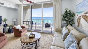 A spacious living room with a balcony overlooking the ocean, furnished with a sofa, armchairs, and a coffee table.