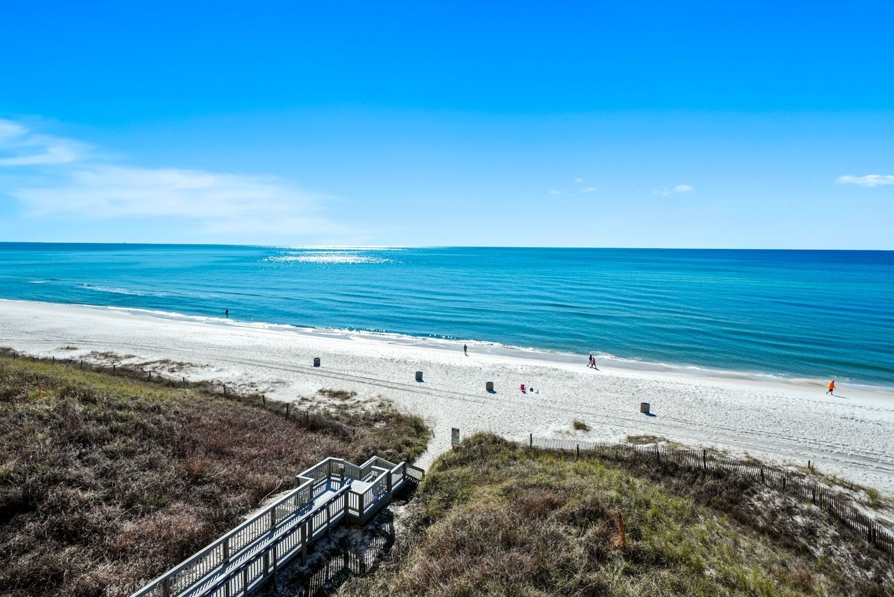 Ein Strand mit einer Holzpromenade, die zum Ufer führt, feinem Sand und ruhiger See.