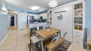 A modern kitchen with white cabinets, a central island, and a dining area with a wooden table and chairs. - Sea-horsey 3 Bedroom Condo by RedAwning (Panama City Beach)