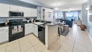 A modern kitchen with white cabinets, a black stove, and a large island with a sink. - Sea-horsey 3 Bedroom Condo by RedAwning (Panama City Beach)