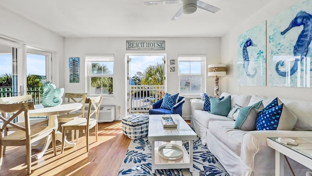 Amplia sala de estar con una mesa de comedor, sillas, un sofá y una mesa de centro. Se observa un letrero que dice "BEACH HOUSE", lo que indica una decoración temática de playa.