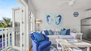 Un salón moderno con un sillón azul, sofá blanco y alfombra estampada. Hay dos obras de arte en la pared y un reloj.