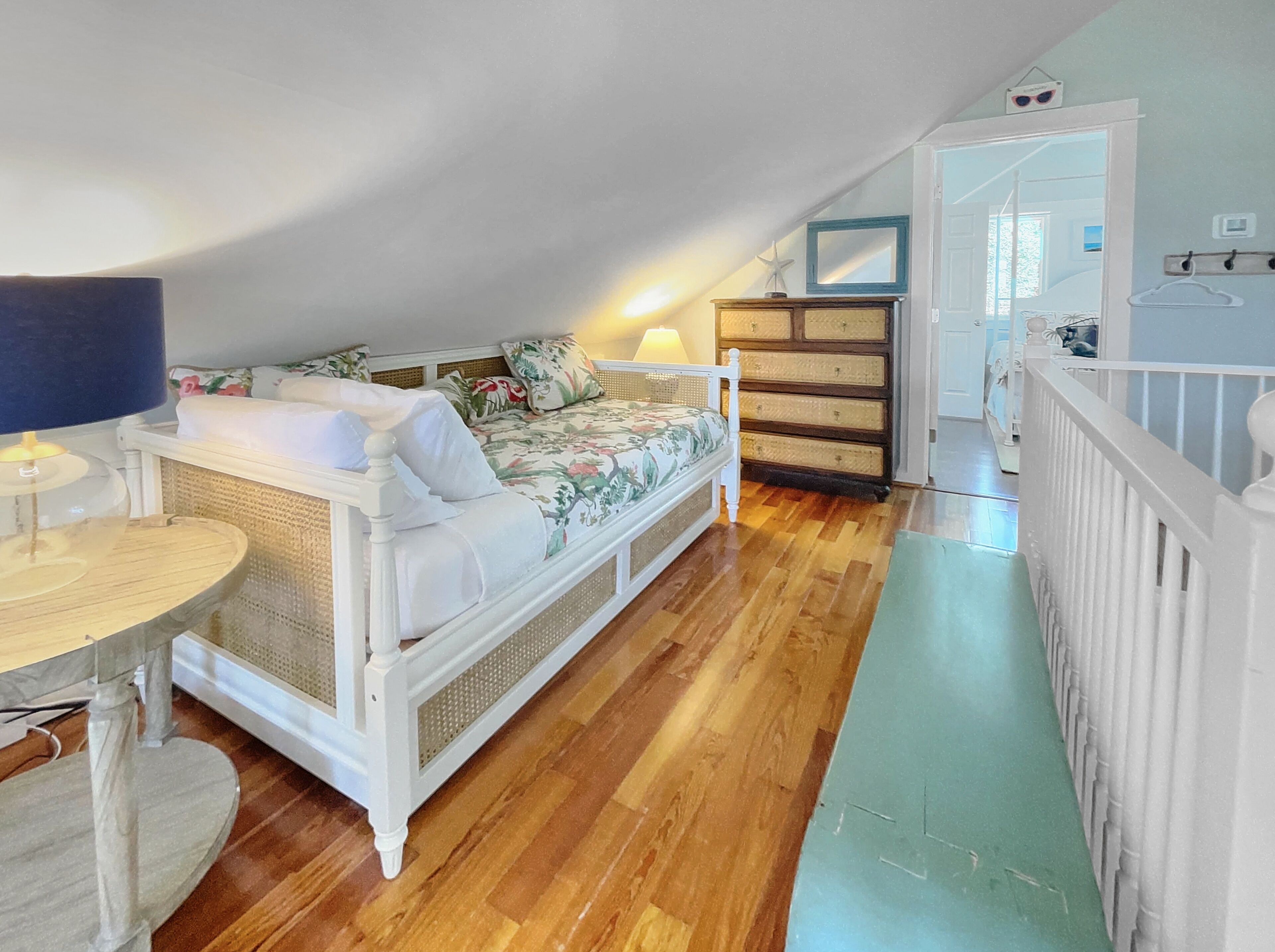 A bedroom with a bed, a dresser, a lamp, and a view of the hallway.