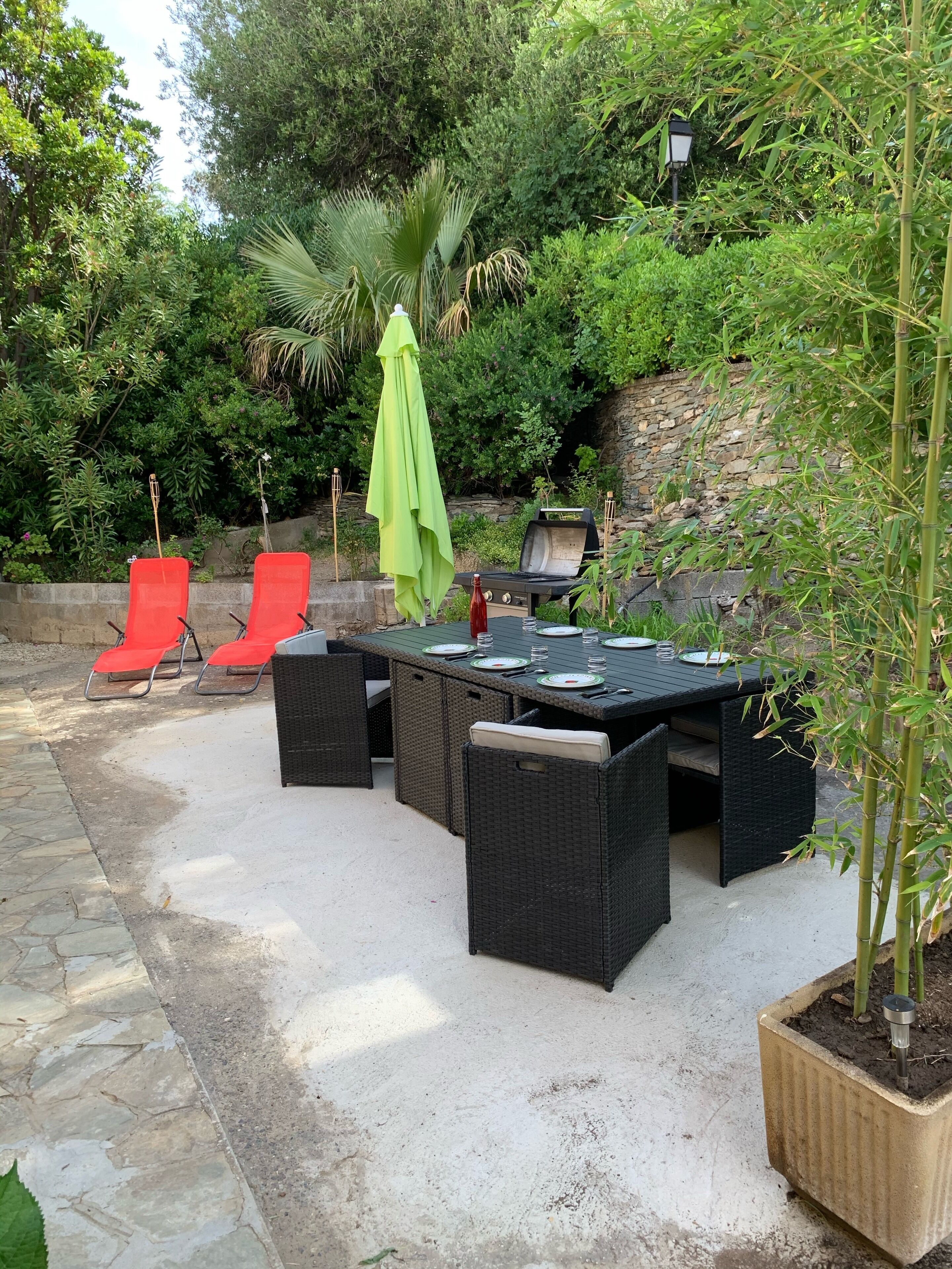 Eine Terrasse im Freien mit Esstisch und Stühlen, umgeben von üppiger Vegetation und einer Steinsäule.