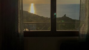 A room with a large window overlooking a sunset over the sea.