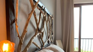 A bedroom with a wooden headboard, a bedside lamp, and a view of the outdoors.