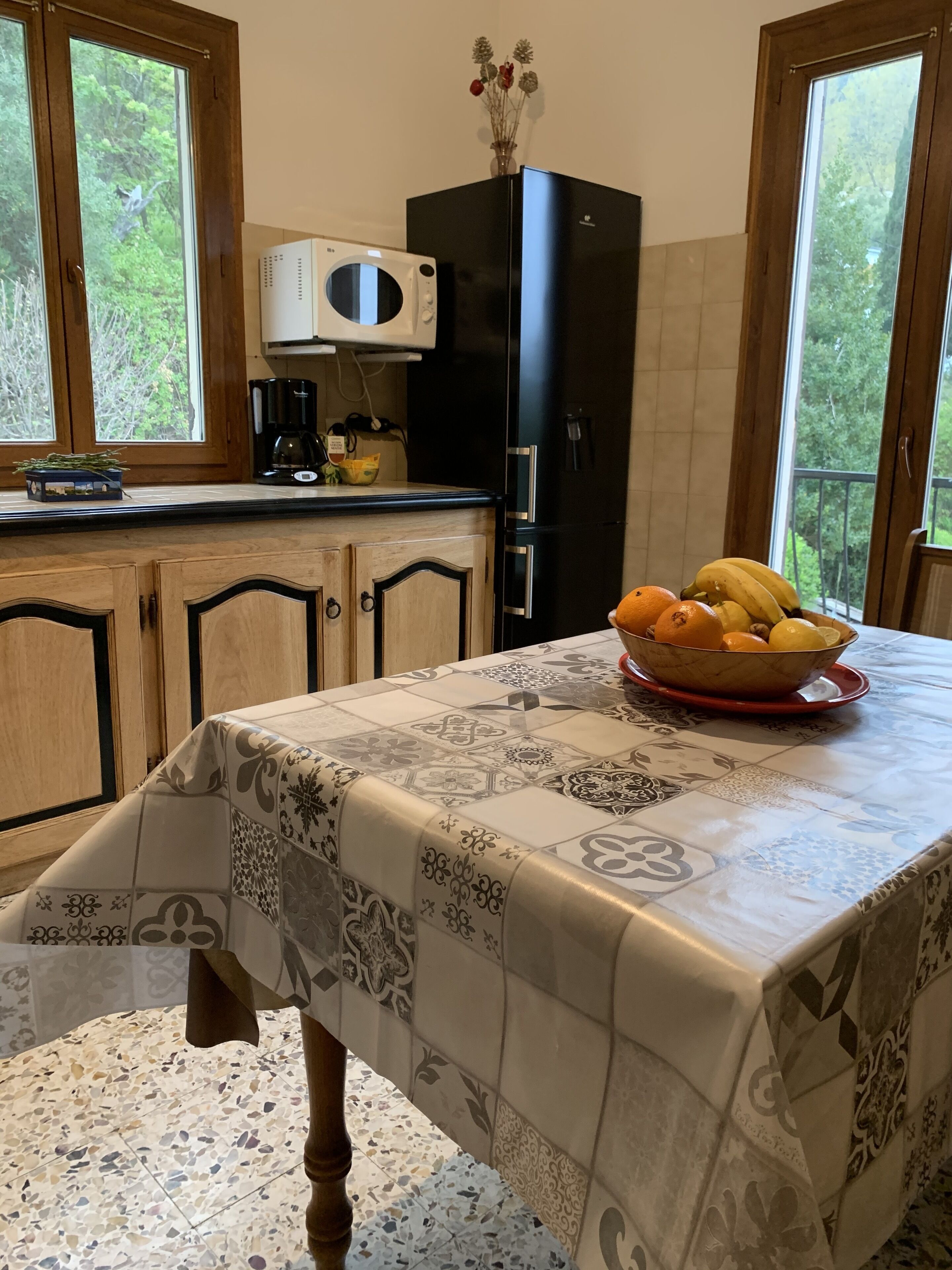 Une cuisine avec une table mise pour le petit-déjeuner, un réfrigérateur noir et une fenêtre donnant sur des arbres.