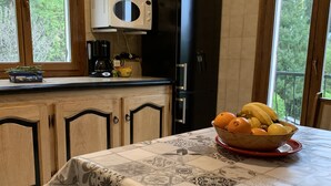 A kitchen with a table set for breakfast, a black refrigerator, and a window with a view of trees.
