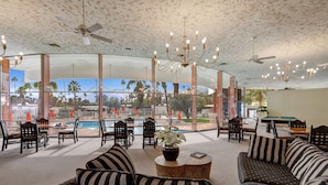 A spacious lounge area with a pool view, comfortable seating, and a chandelier. - Posh Condo in Ocotillo Lodge in South PS (Palm Springs)