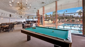 A pool table in a room with large windows overlooking a pool and palm trees. - Posh Condo in Ocotillo Lodge in South PS (Palm Springs)