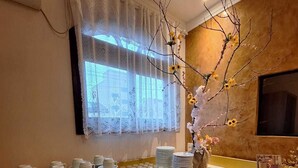 A kitchen with a wooden countertop, a window with lace curtains, and a vase with branches and flowers. - Pousada Estrela Dalva (Penha)