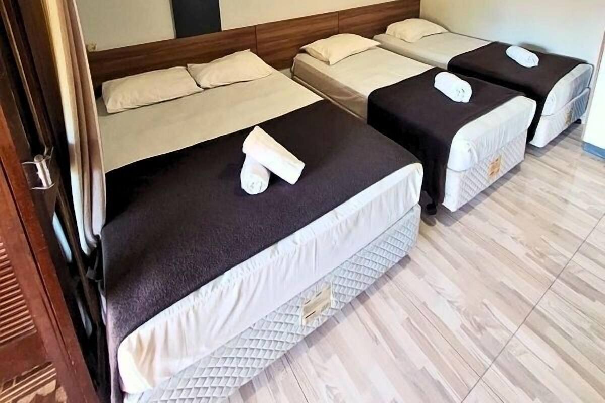 Quarto de hotel com três camas, cada uma com travesseiro e toalha.