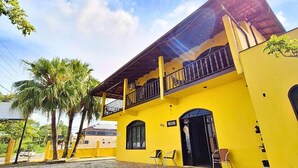 A yellow building with a balcony, stone-paved courtyard, and palm trees. - Pousada Estrela Dalva (Penha)