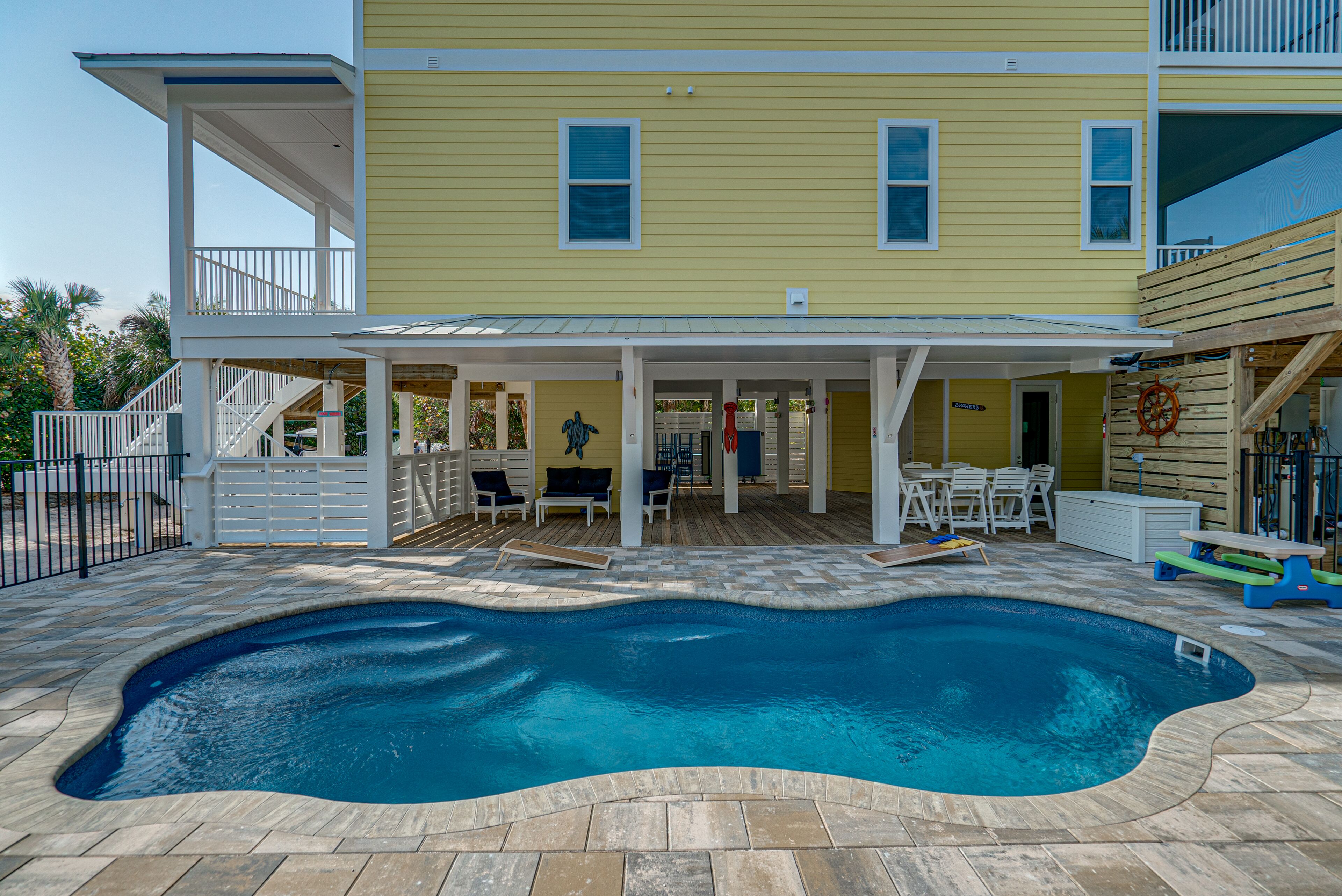 Una casa amarilla de dos pisos con piscina, muebles de exterior y un patio cubierto.