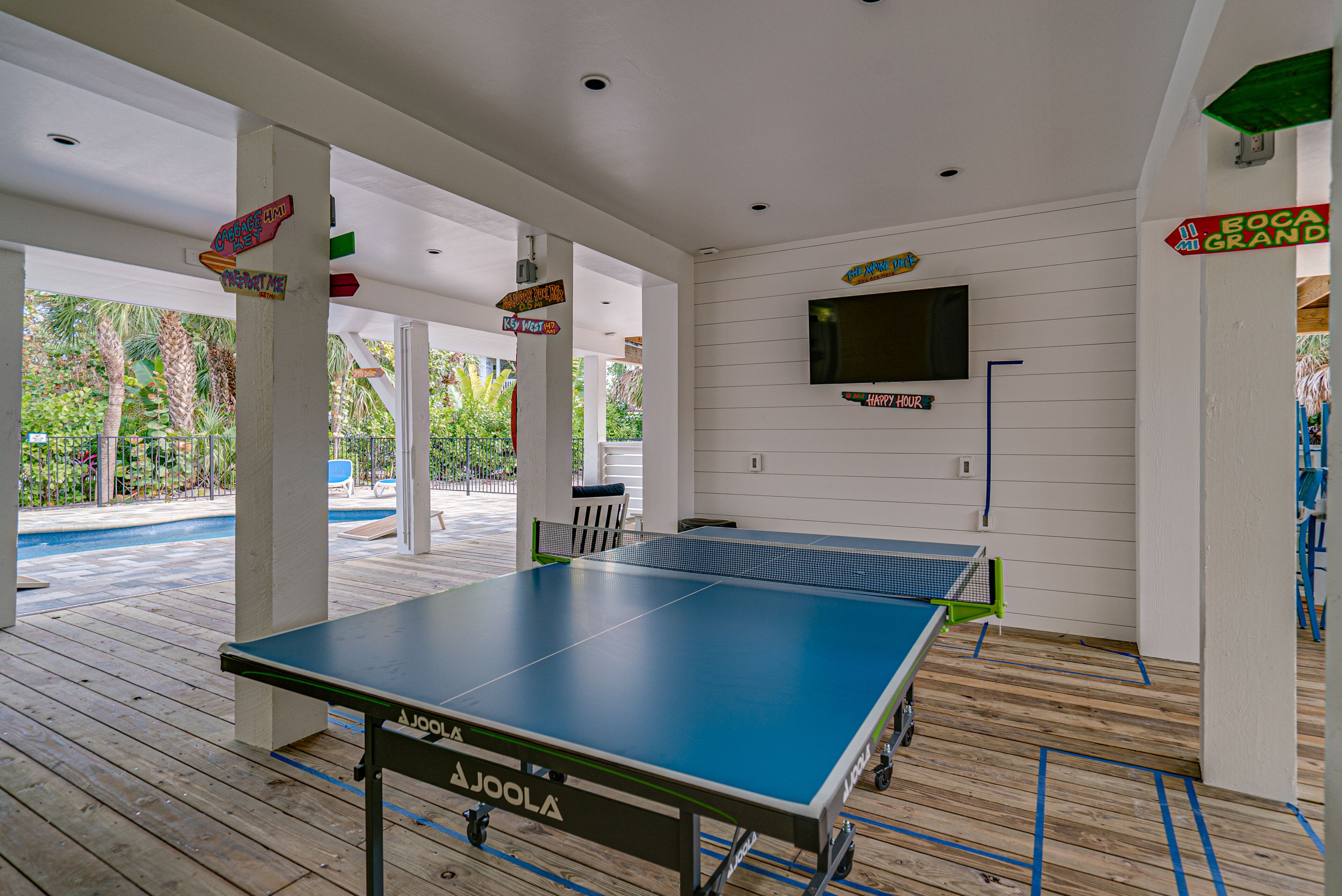 Uma mesa de ping pong em área coberta, com placas de sinalização e uma televisão na parede.