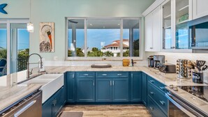 Een moderne keuken met blauwe kastjes, een groot raam en uitzicht op een huis.