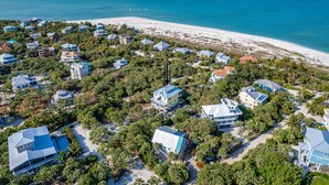 Luchtbeeld van een kustgebied met woonhuizen, weelderige begroeiing en een strand.