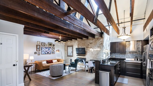Een ruime woonkamer met een bank, salontafel en televisie, een keuken met moderne apparatuur, en zichtbare houten balken.