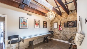 Een biljarttafel met stoelen, een kroonluchter, een gitaar en dartborden in een kamer met zichtbare bakstenen muren en houten balken.
