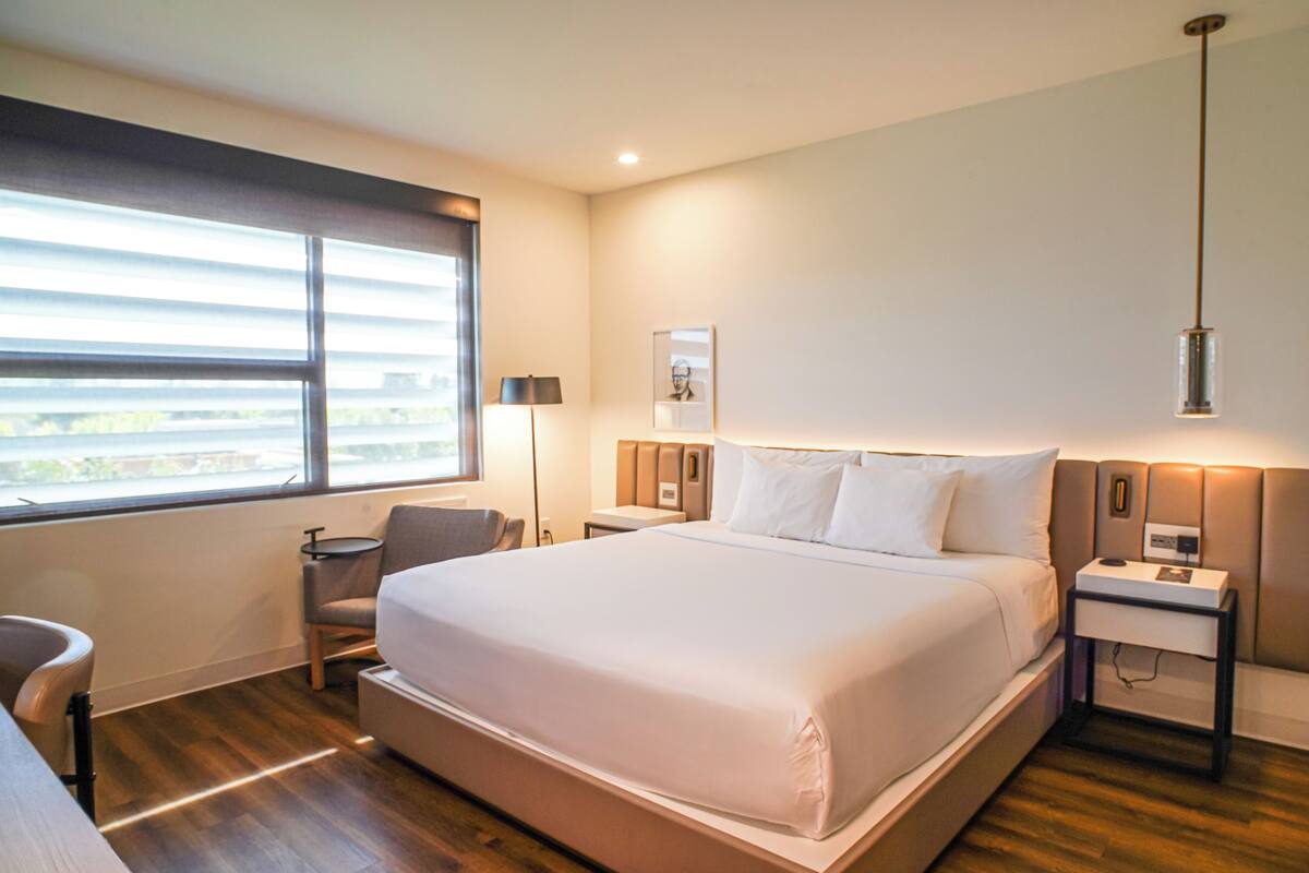 Ett modernt hotellrum med en stor säng, ett skrivbord, en stol och ett fönster med persienner.