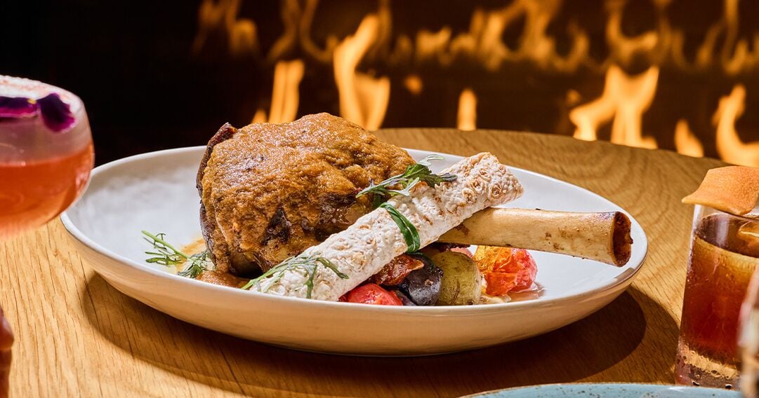 A plate of food with a roasted meat, vegetables, and a bread roll on a wooden table.