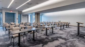 Una sala conferenze con diversi tavoli e sedie, pavimento con moquette e ampie finestre.