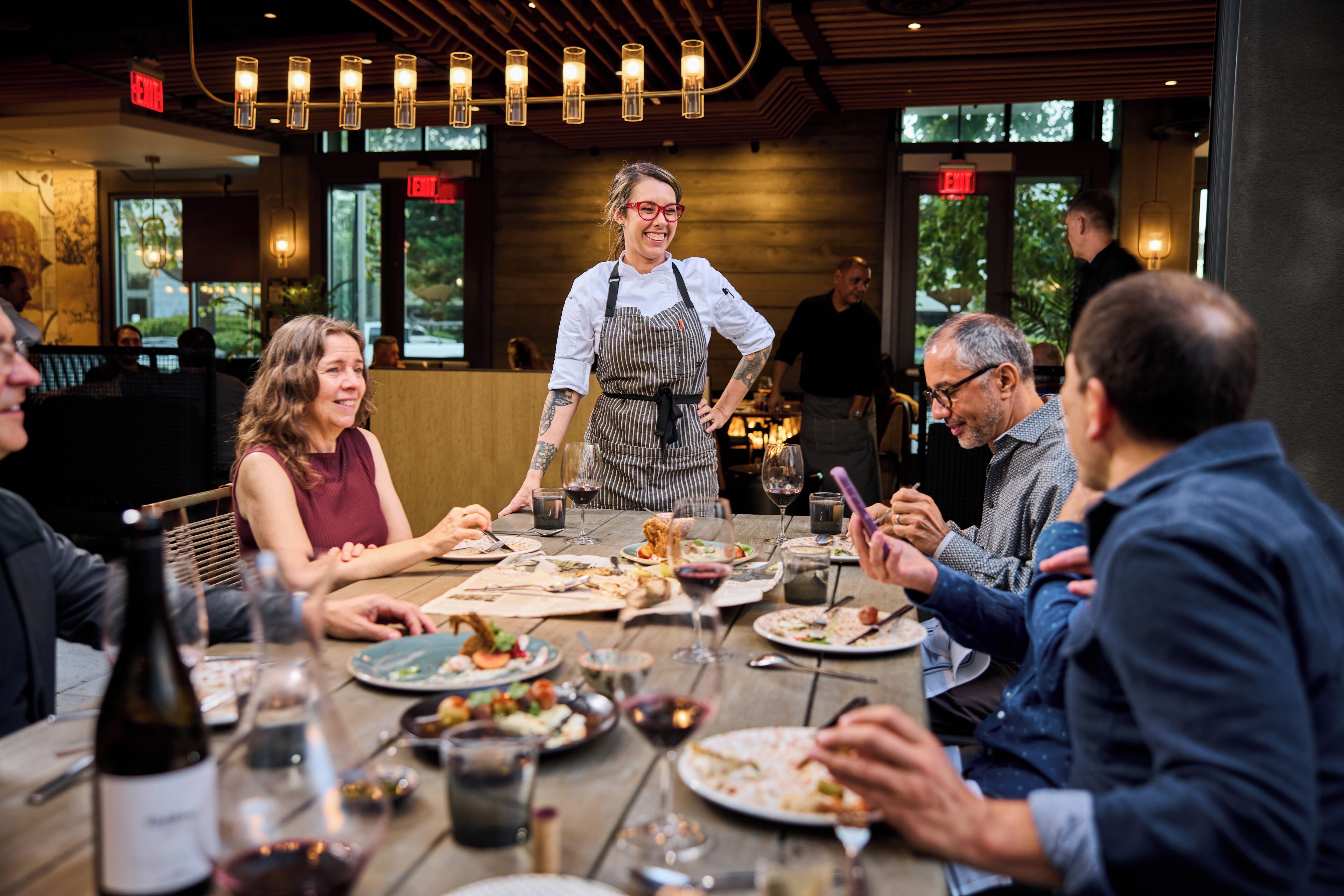 A restaurant with wooden tables, diners, and a waiter serving food.