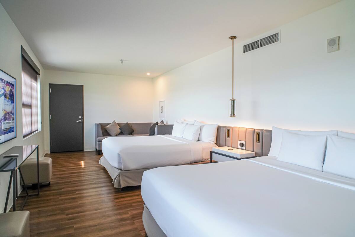 Ett hotellrum med två sängar, ett skrivbord, en stol, en tv och en dörr.