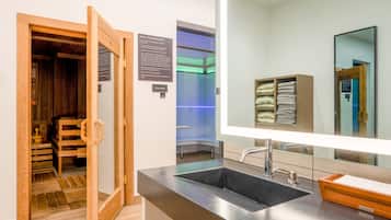 Enjoy a refreshing sauna experience in this bathroom, featuring a large mirror and a door leading to a sauna room with a bench and towel rack.