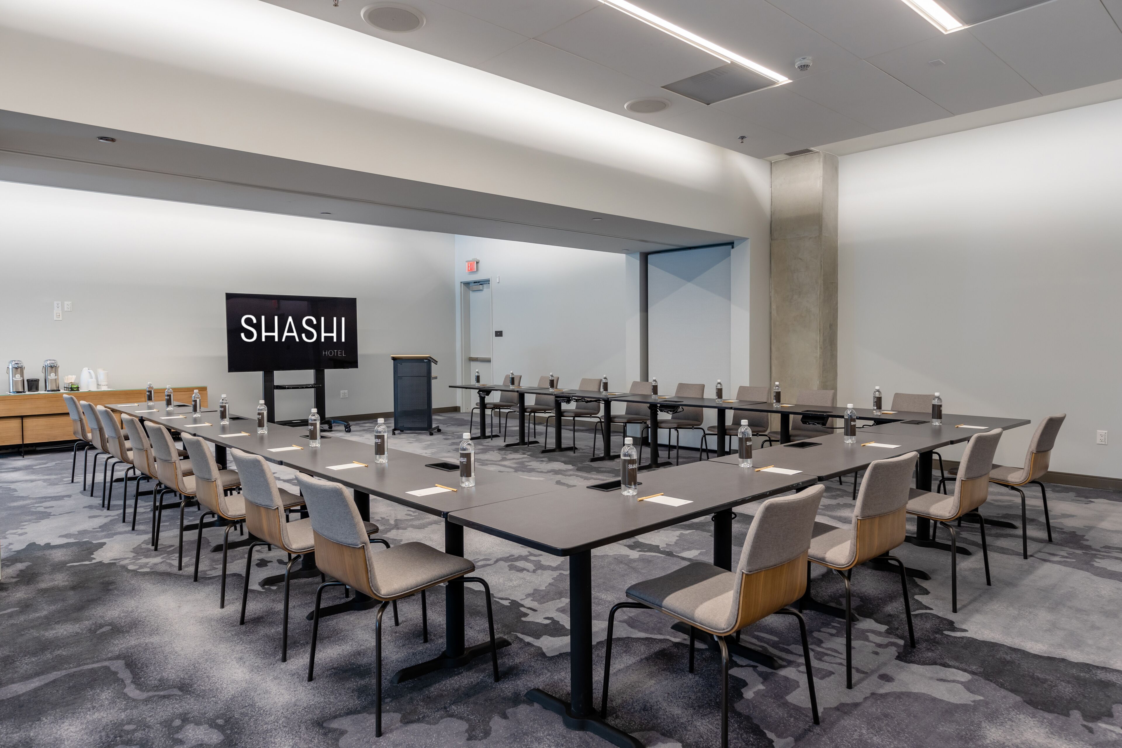 A conference room with long tables and chairs, a flat-screen TV, and a sign that reads "SHASHI HOTEL".