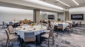 A conference room with round tables set for dining, a large screen displaying "SHASHI HOTEL", and a modern interior design.