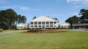 A large, white building with a central portico and columns, surrounded by a well-maintained lawn and trees. - Beautiful Second Floor 2-Bedroom Two-Bath Condo With Water and Golf Views (Calabash)