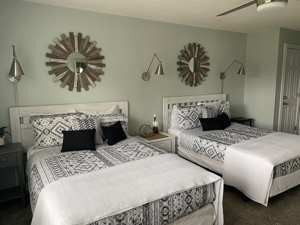 Een slaapkamer met twee bedden, elk voorzien van beddengoed met een patroon en een passend hoofdbord. Er hangen spiegels aan de muur en er staan bedlampen op de nachtkastjes.