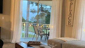 A living room with a dark wooden coffee table, a beige sofa, and a view of a balcony with string lights. - Beautiful Second Floor 2-Bedroom Two-Bath Condo With Water and Golf Views (Calabash)