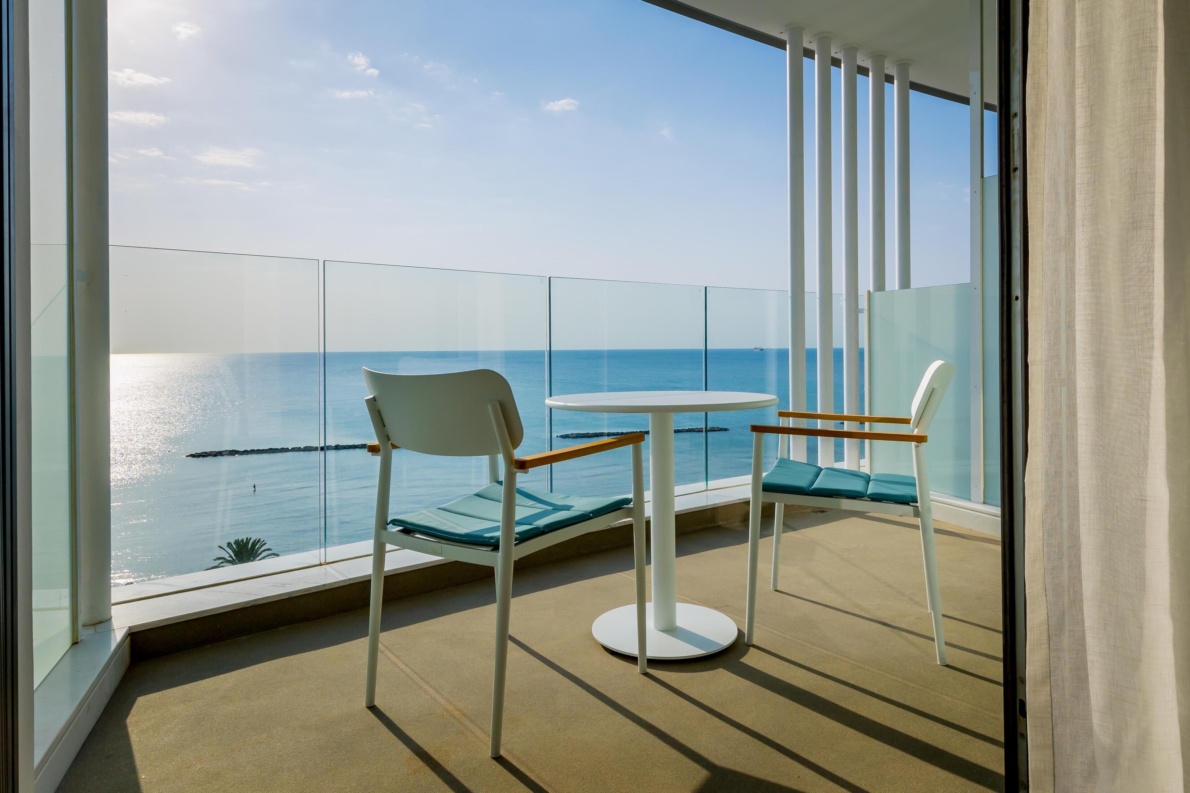 A balcony with a table and chairs, overlooking a body of water.