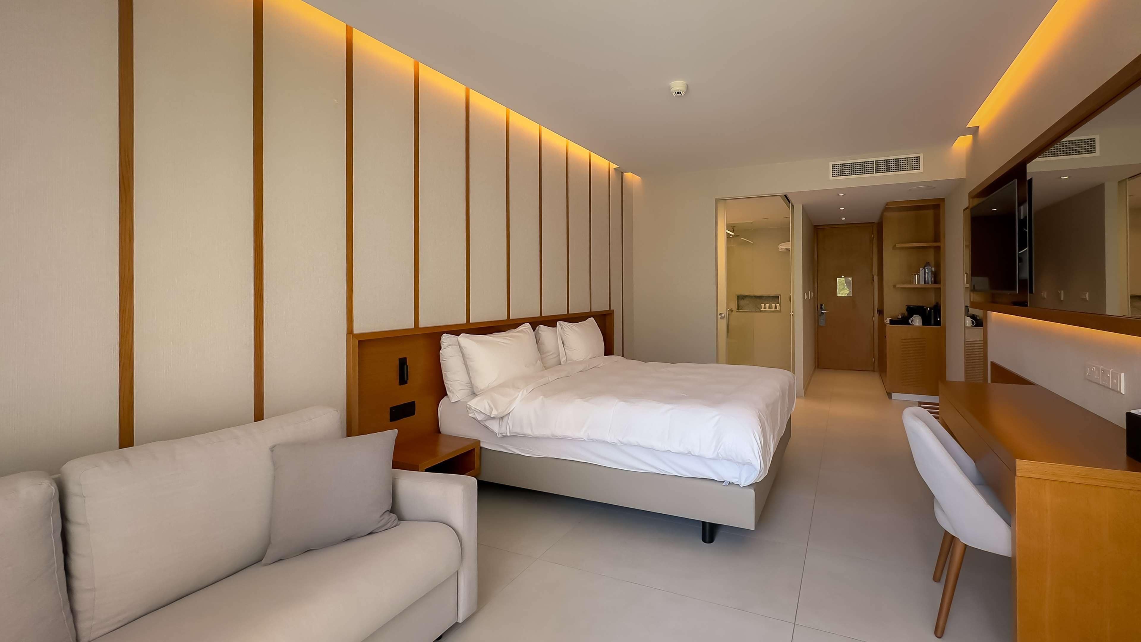 A modern hotel room with a bed, a sofa, a desk, and a TV.
