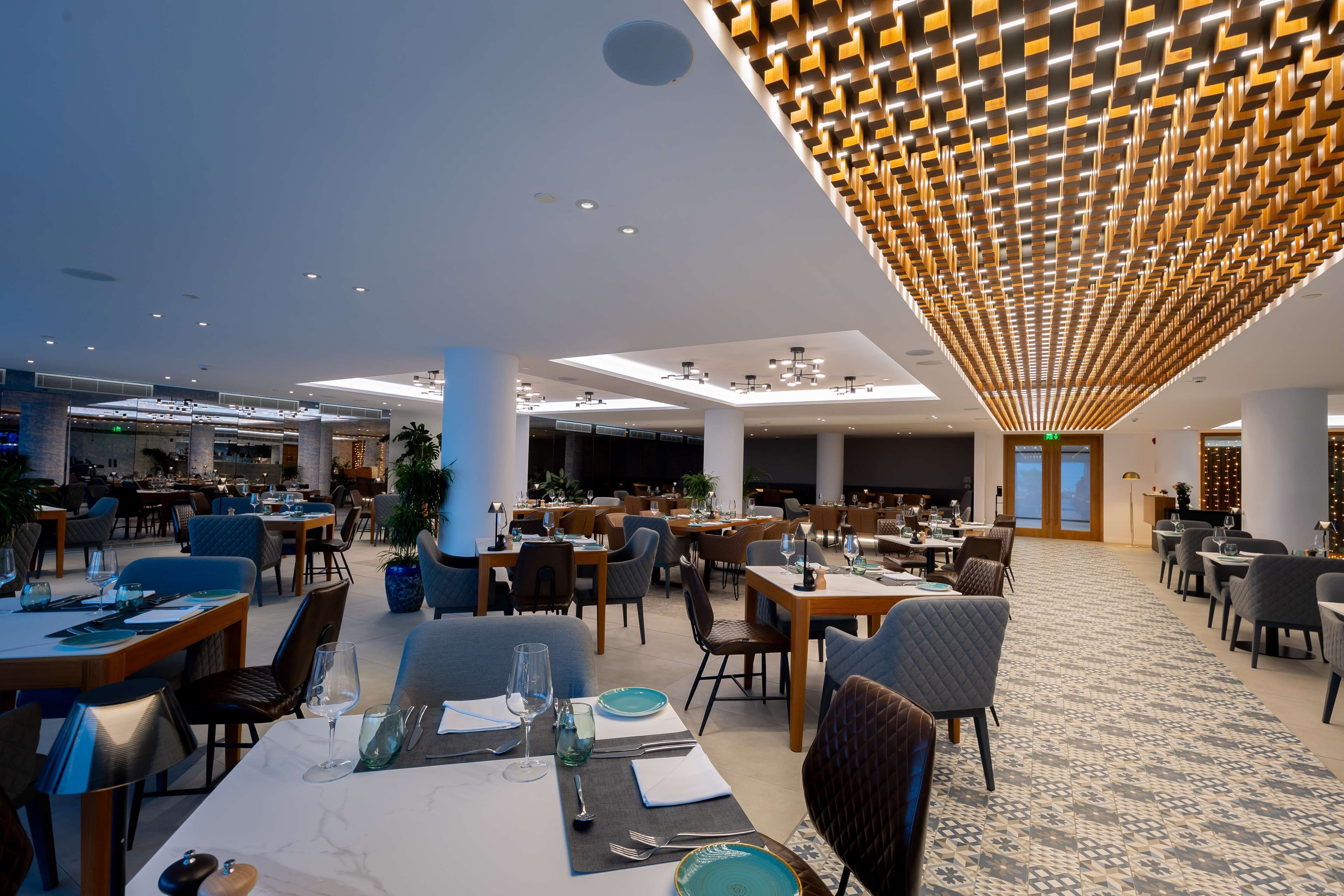 A spacious dining area with multiple tables and chairs, a patterned ceiling, and a view of the dining area in the background.