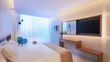 A modern hotel room with a large bed, a blue chair, a small table with fruit, and a TV mounted on the wall.