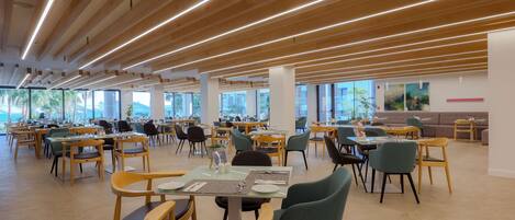 Un amplio comedor con mesas y sillas de madera, ventanas grandes y un diseño moderno en el techo.