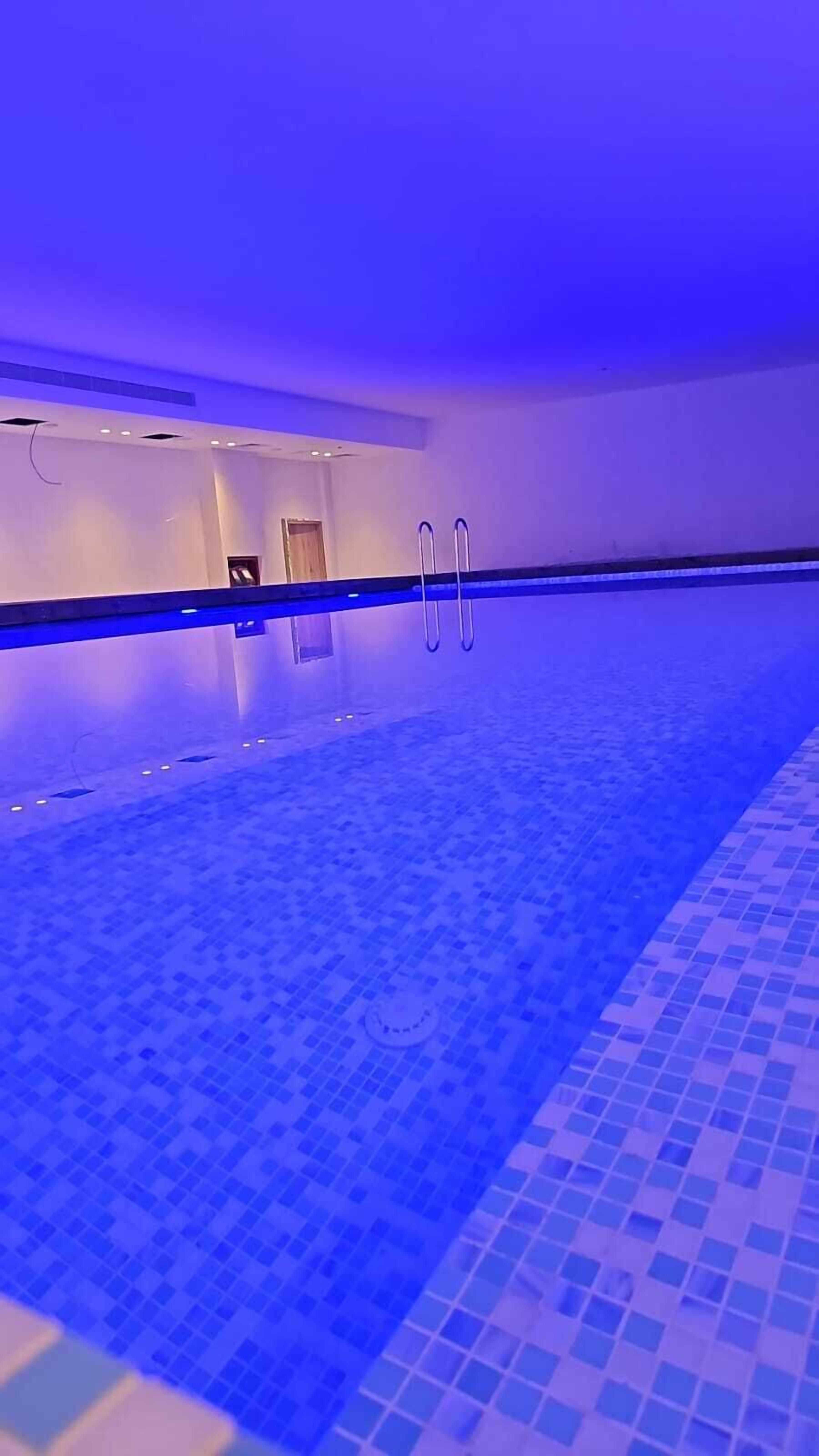 A swimming pool with a blue tiled floor and walls, and a door leading to another room.