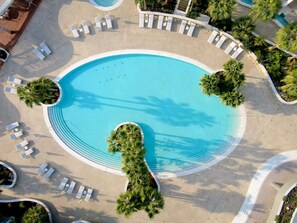 An aerial view of a circular pool surrounded by white lounge chairs and palm trees.
