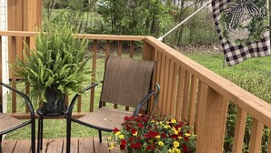 Een houten terras met een stoel en een tafel, omgeven door groen en een 'Welcome' bord.