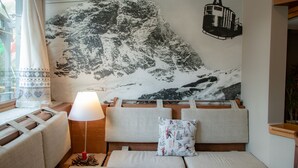 Ein gemütliches Zimmer mit Bergbild, einer gepolsterten Bank, einer Lampe und einem Fenster mit Vorhängen.