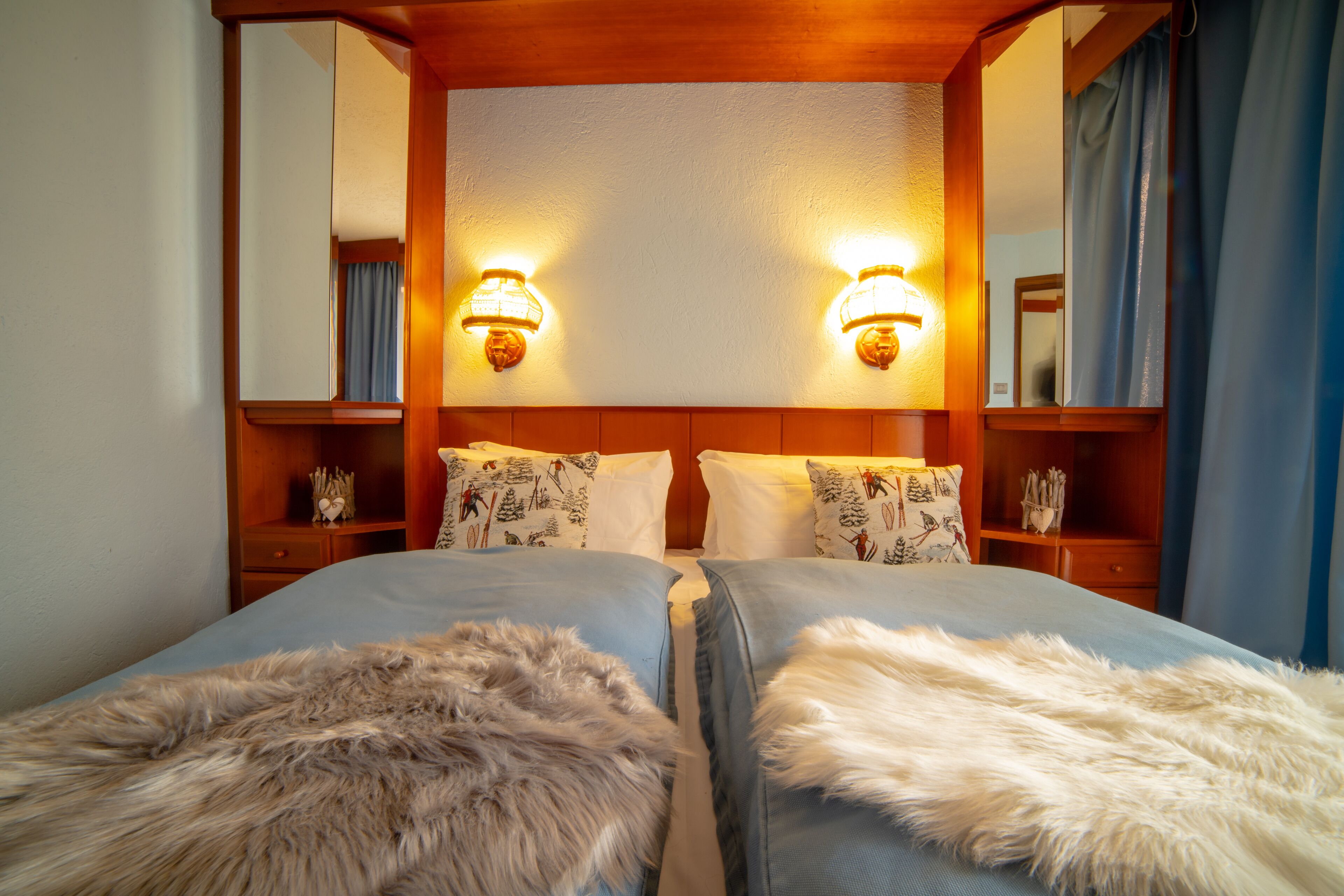 Ein Hotelzimmer mit zwei Betten, einem Holzkopfstück, Wandlampen und einem Spiegel.