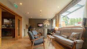 Ein geräumiger Wohnbereich mit einer Couch, Sesseln, einem Fernseher und einem großen Fenster mit Blick ins Freie.