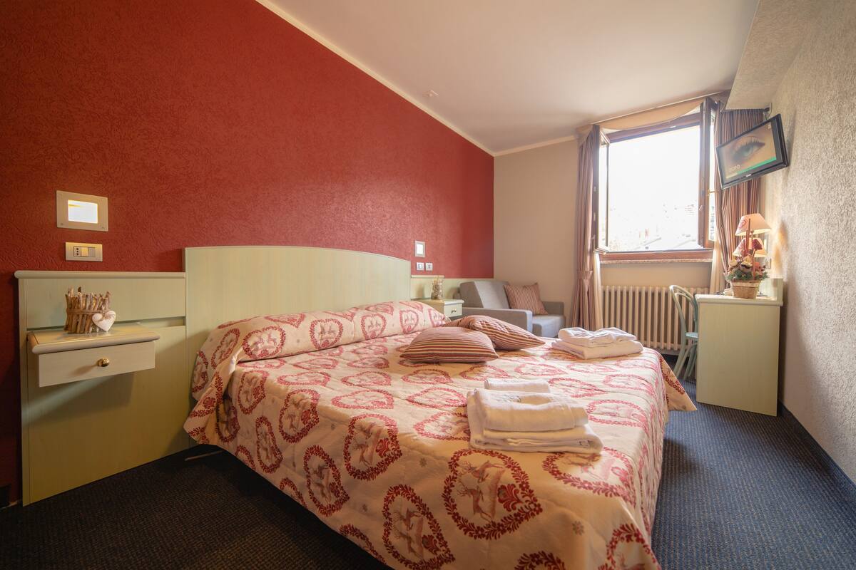 Ein Hotelzimmer mit einem Bett, einem Schreibtisch, einem Sessel, einem Fenster und einem Fernseher.