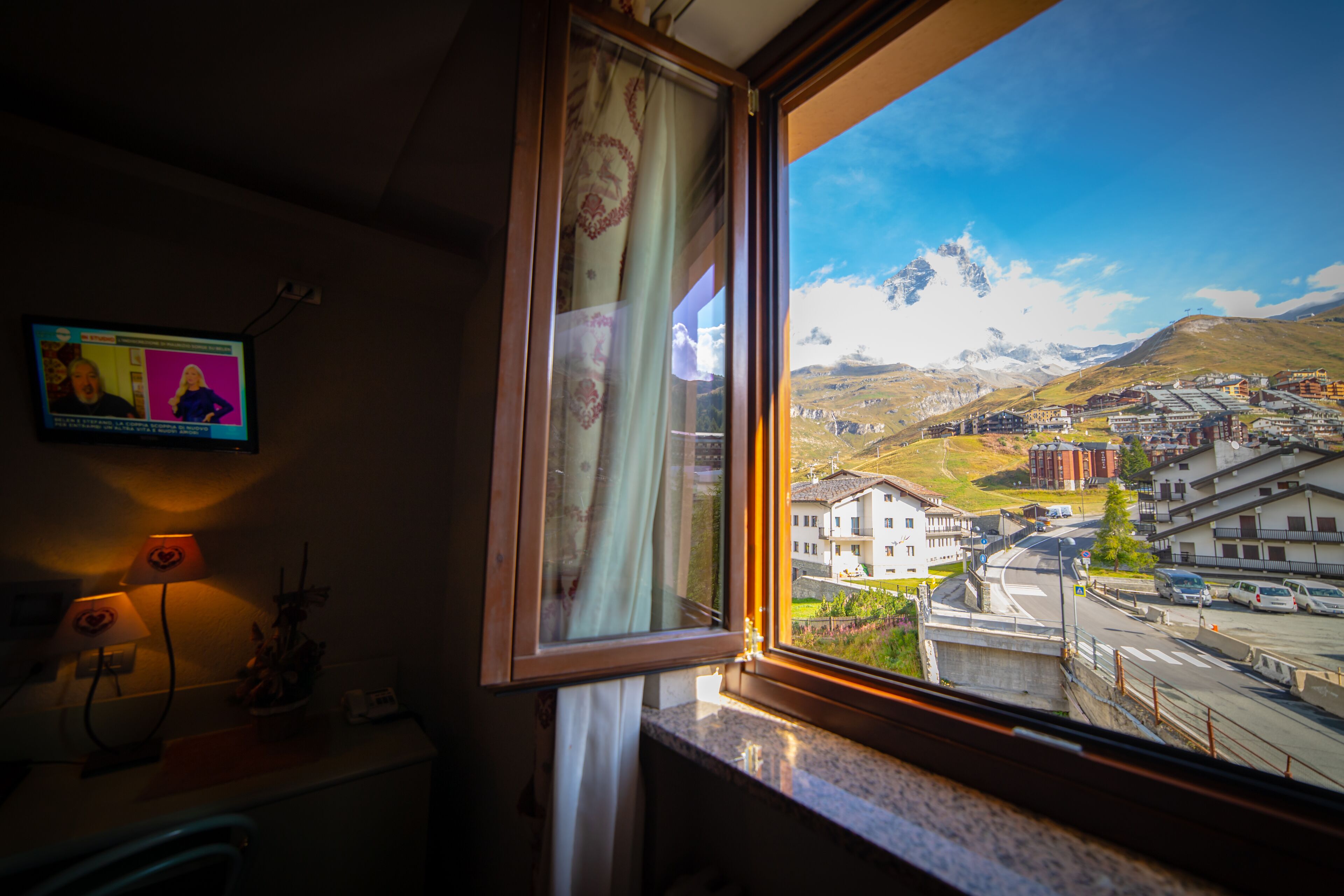 A room with a window overlooking a town and mountains.