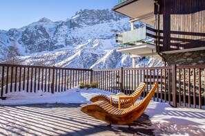 Une terrasse en bois dotée de chaises au design original, un mur en pierre et une vue sur des montagnes enneigées.